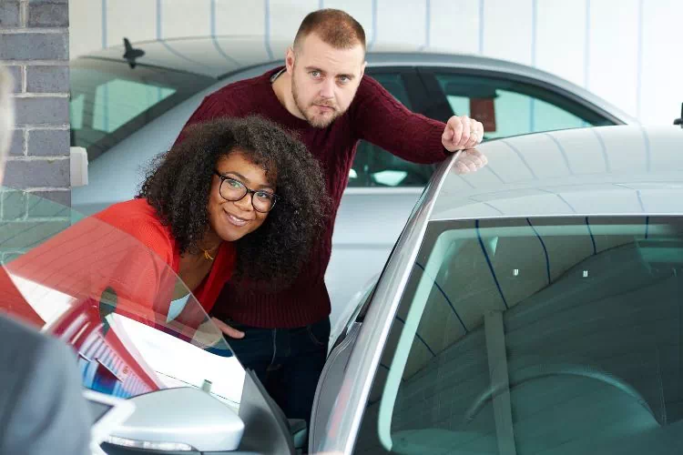 Jeune couple en train d'inspecter une voiture d'occasion avant de l'acheter