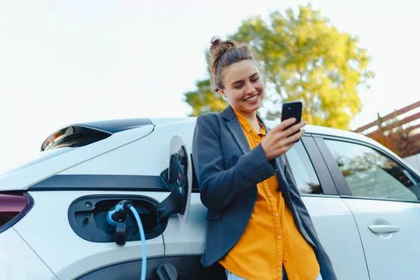 Jeune femme appuyée sur sa voiture qui recharge